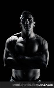 Low light portrait of bodybuilder with crossed hands over black background