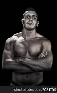 Low light portrait of bodybuilder with crossed hands over black background