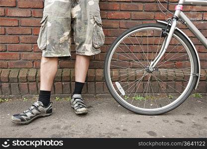 Low section of biker standing with bicycle