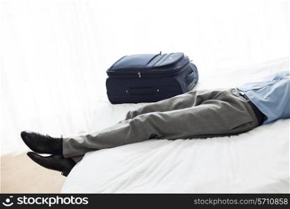 Low section of businessman sleeping beside luggage in hotel room