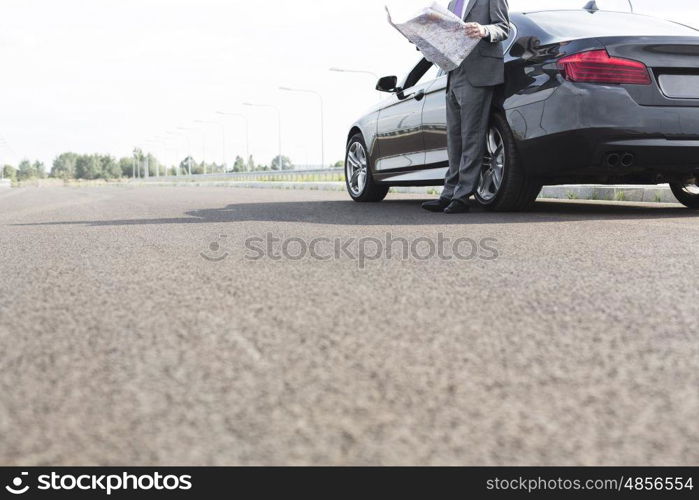 Low section of businessman with map while standing outside car on road