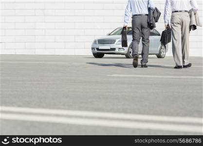 Low section of businessmen carrying briefcases while walking towards car on street