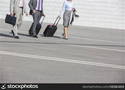Low section of businesspeople with luggage walking on street