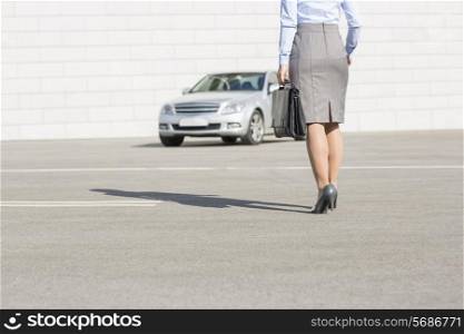 Low section of businesswoman carrying briefcase while walking towards car on street