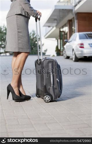 Low section of businesswoman standing with suitcase on driveway
