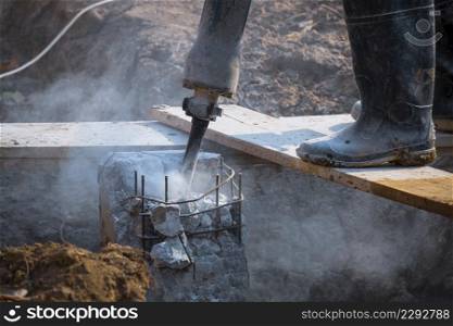 Low section of construction worker using jackhammer drill equipment to breaking reinforced concrete pillar in construction site