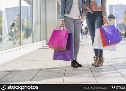 Low section of female friends holding shopping bags on sidewalk