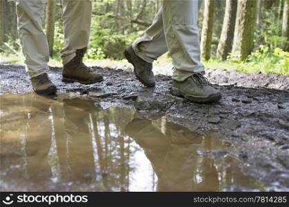 Low section of hikers walking through a mud puddle in forest