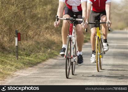 Low section of male athletes riding bicycles on a country road