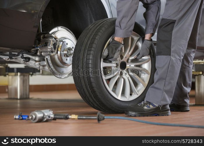 Low section of male mechanic repairing car&rsquo;s tire in repair shop