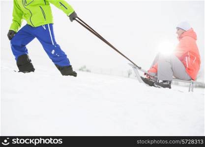 Low section of man giving sled ride to woman in snow