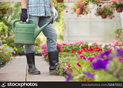 Low section of man holding watering can at greenhouse