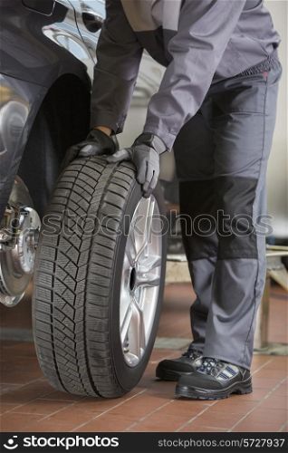 Low section of repairman fixing car&rsquo;s tire in workshop