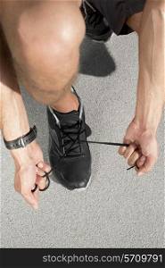 Low section of sporty man tying shoelace on street
