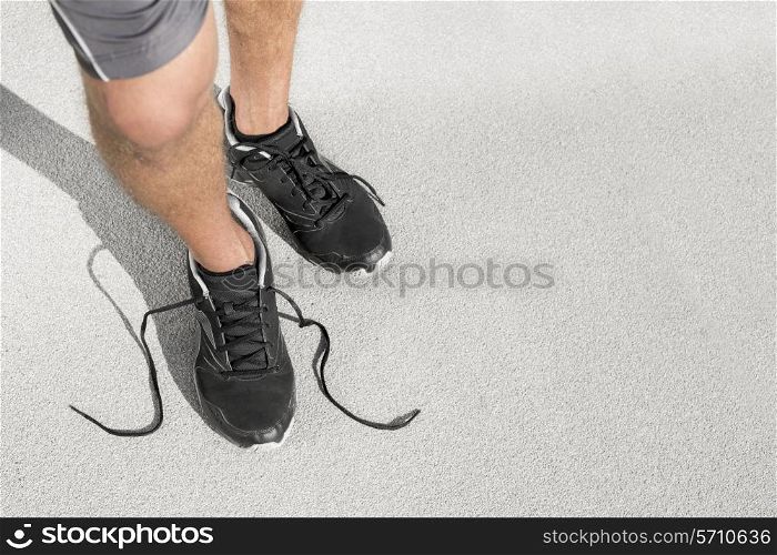 Low section of sporty man with untied shoelace standing on street
