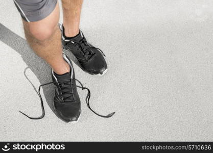 Low section of sporty man with untied shoelace standing on street