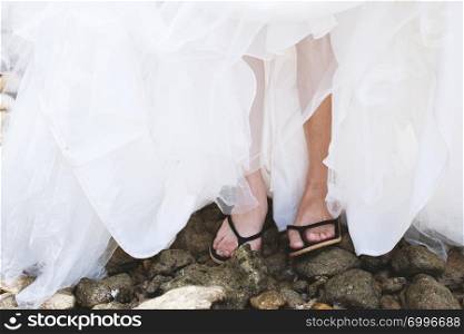 Low section of the bride in slipper on the pebble stones on the beach