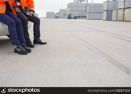 Low section of workers leaning on car in shipping yard