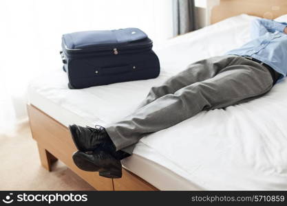 Low section of young businessman sleeping beside suitcase in hotel room