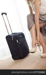 Low section of young businesswoman removing high heels in hotel room