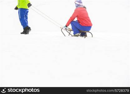 Low section of young man pulling woman on sled