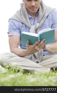Low section of young man reading book on grass