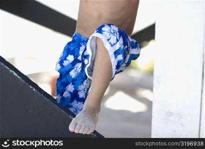 Low section view of a boy standing with his one leg on a railing