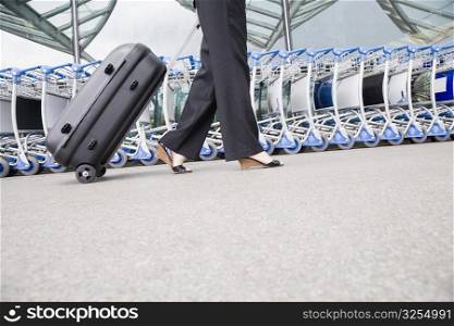Low section view of a businesswoman pulling luggage outside an airport