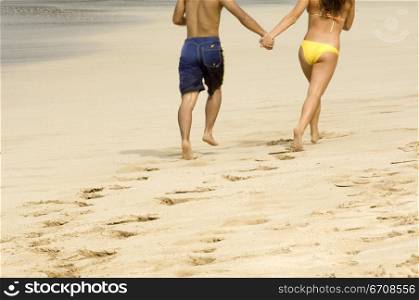 Low section view of a couple running on the beach