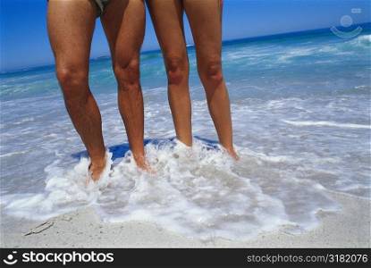 Low-section view of a couple standing in water on the beach