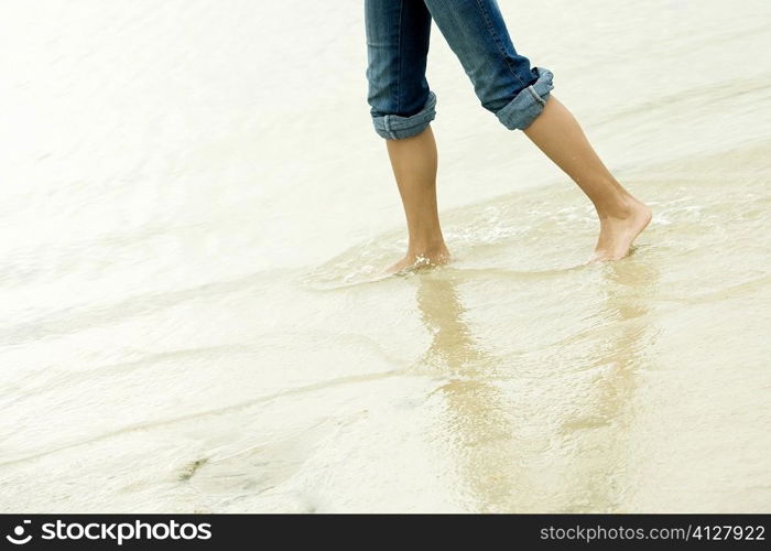 Low section view of a girl wading in water on the beach