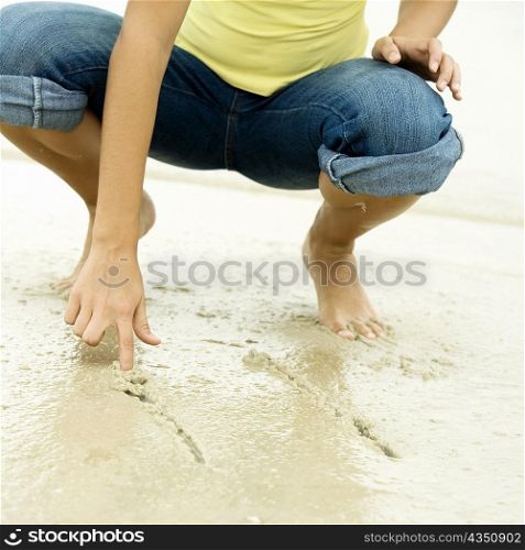 Low section view of a girl writing in sand with her finger