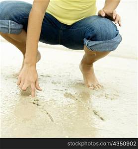 Low section view of a girl writing in sand with her finger