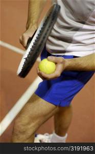 Low section view of a man holding a tennis ball and a tennis racket