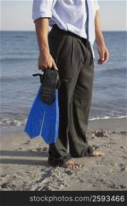 Low section view of a man holding flippers on the beach