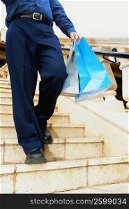 Low section view of a man moving down on steps and carrying shopping bags