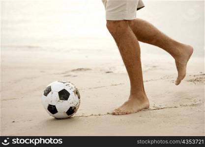 Low section view of a mid adult man playing soccer on the beach