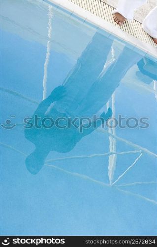 Low section view of a mid adult man standing at the edge of a swimming pool