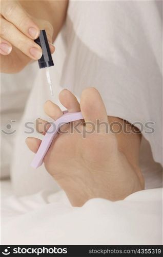 Low section view of a mid adult woman applying nail polish on her toenails