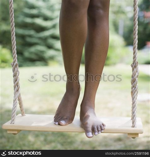 Low section view of a mid adult woman standing on a rope swing