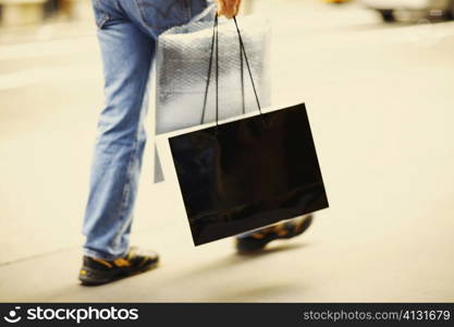 Low section view of a person walking and carrying a shopping bag