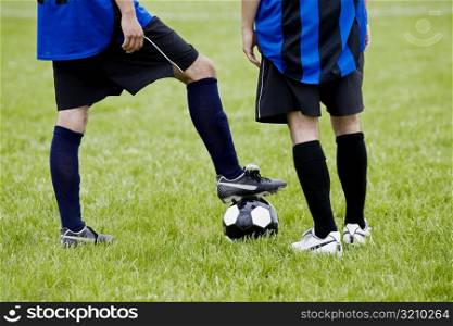 Low section view of a soccer player resting his foot on a soccer ball with another player standing beside him
