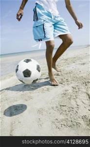 Low section view of a teenage boy playing with a soccer ball on the beach