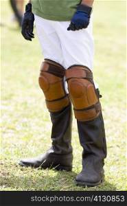 Low section view of a teenage boy wearing riding boots and kneepads