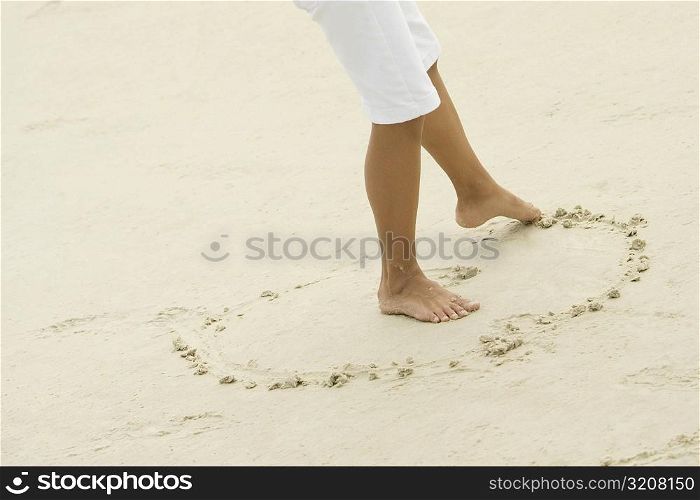 Low section view of a teenage girl drawing in sand with her toe