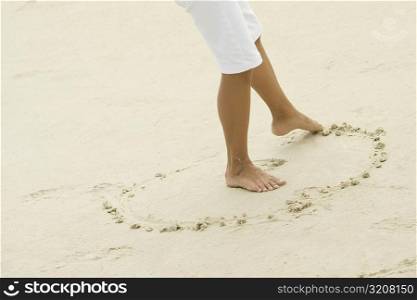 Low section view of a teenage girl drawing in sand with her toe