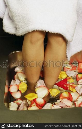 Low section view of a woman&acute;s feet soaked in a tub of flower petals and water