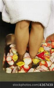 Low section view of a woman&acute;s feet soaked in a tub of flower petals and water