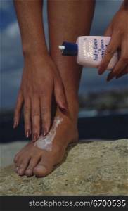 Low section view of a woman applying cream on her foot