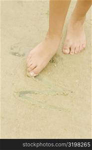 Low section view of a woman drawing in sand with her toe